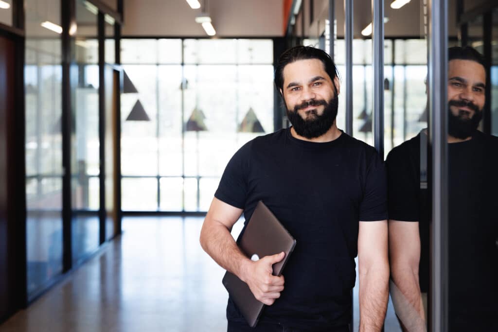 Aboriginal Australian creative director in modern workspace. He is holding a laptop under his arm.