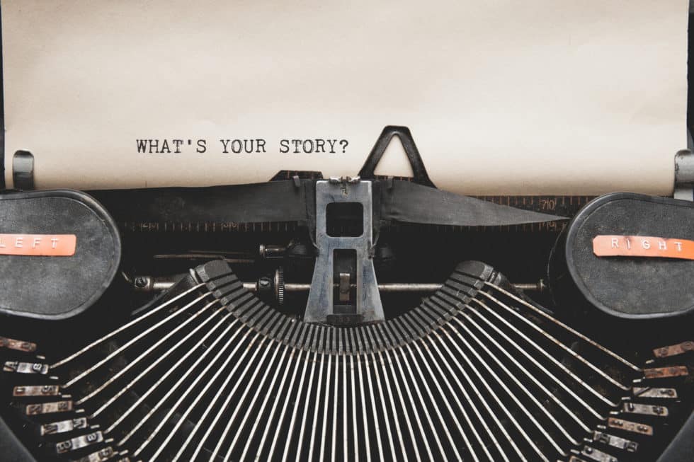 An old typewriter with the question 'what's your story?' typed on a blank page.