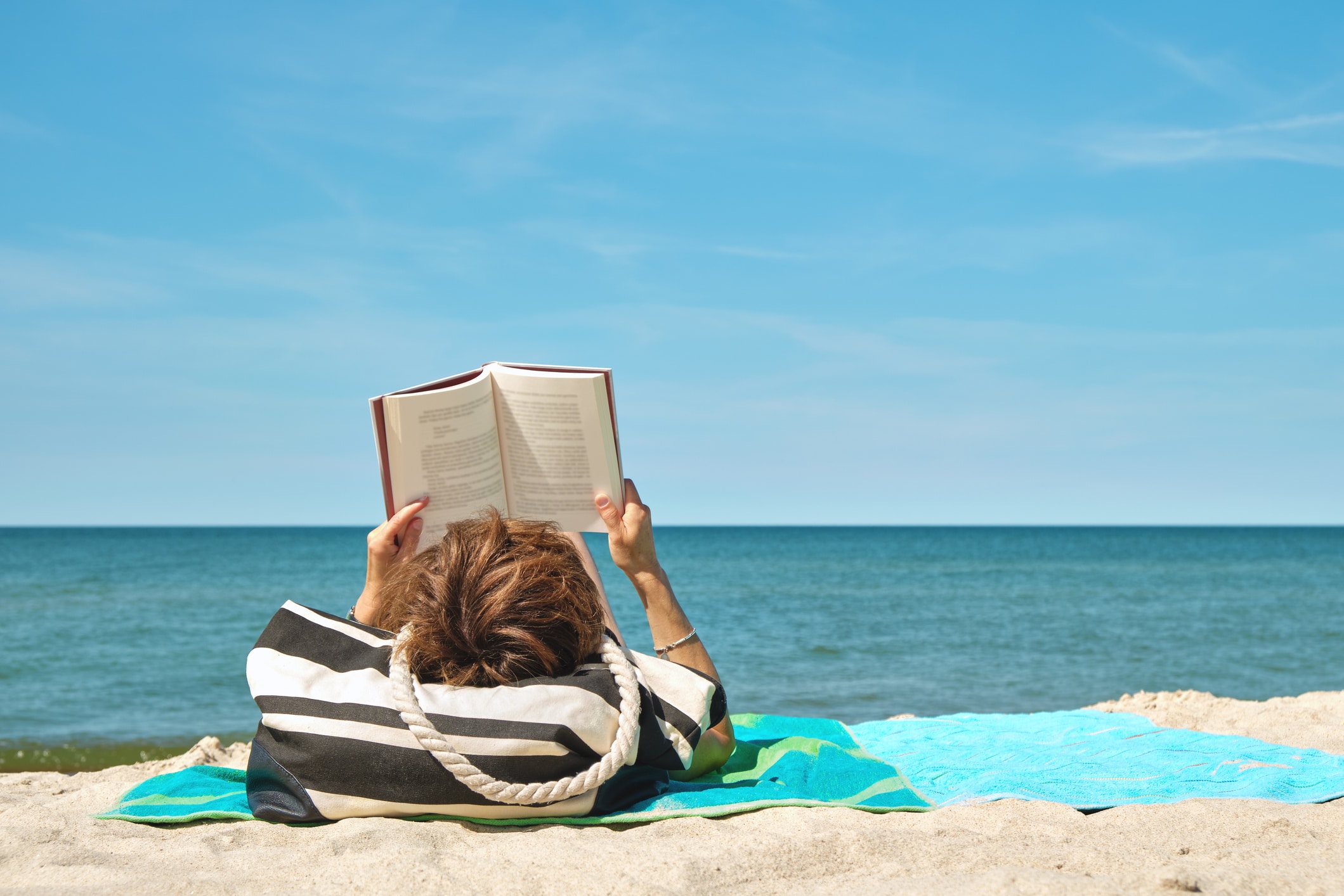 Woman lying on the beach reading a book on bright summer day.