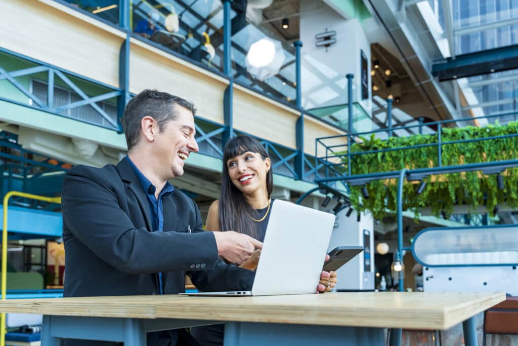 Smiling business man and business woman reviewing a report on a laptop screen in a sustainable office environment.