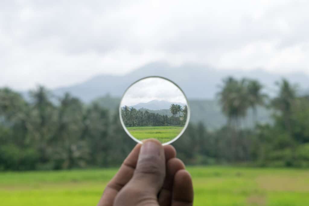 Close up of hand holding a lens, through which you can see a magnified view of a field.