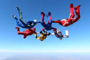 A group of skydivers hold hand in the air demonstrating trust.